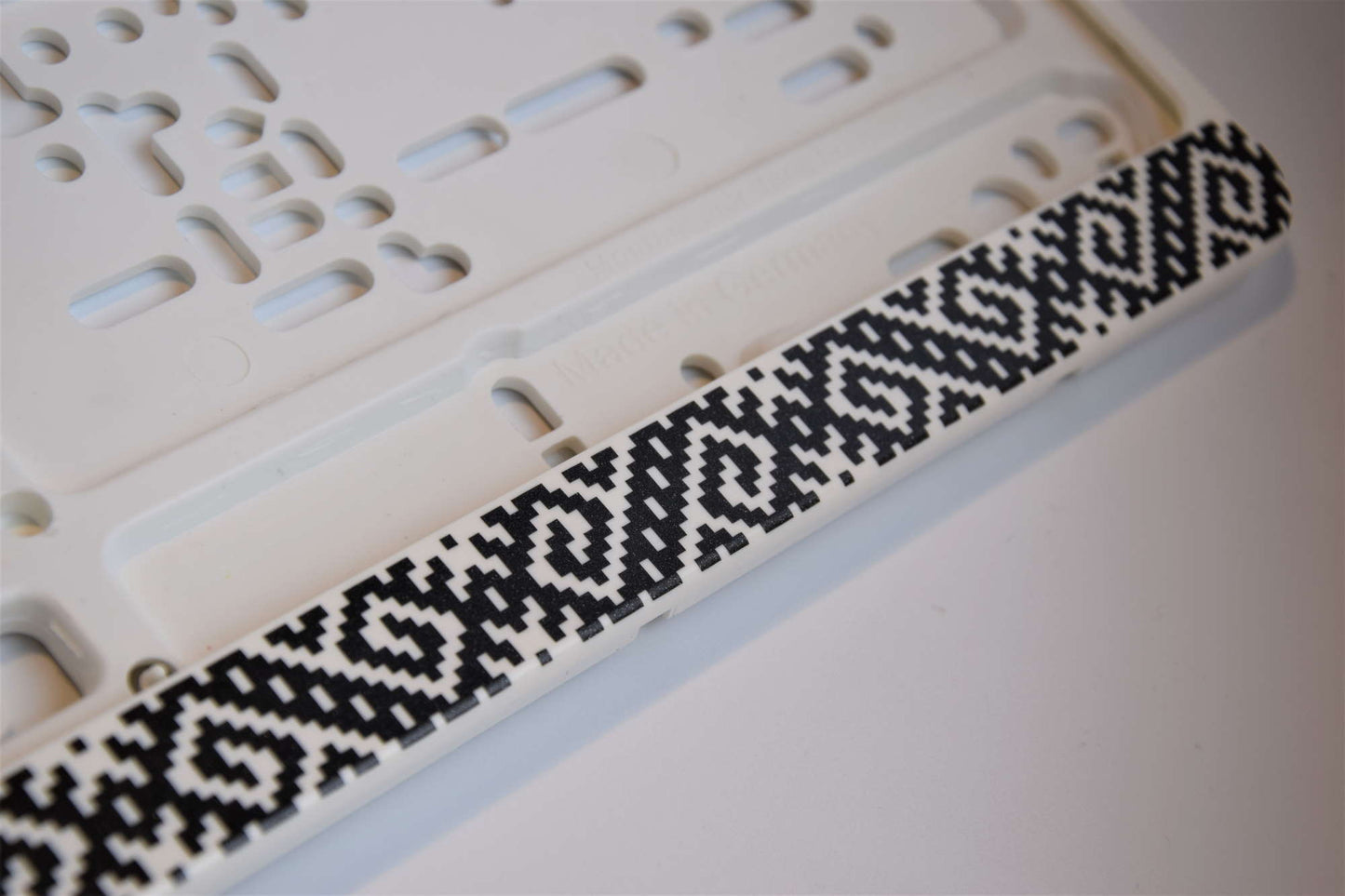 Balts auto numura turētājs ar latviešu rakstiem