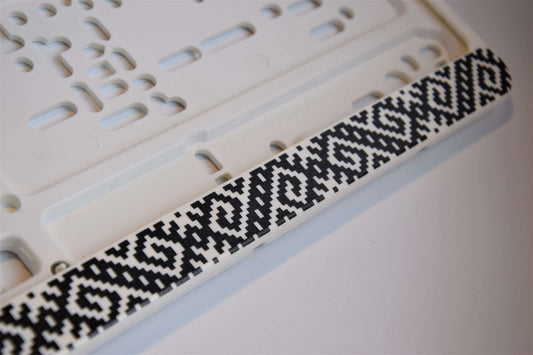 Balts auto numura turētājs ar latviešu rakstiem